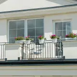 Białe okna pięknie komponują się z jasną, tynkowaną elewacją, tworząc elegancki wygląd. Balkon ozdobiony kwiatami dodaje uroku.