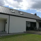 Nowoczesny dom z szarym dachem z blachy na rąbek stojący. Dach wygląda na nowy, bez widocznych wad, z dwoma oknami dachowymi.