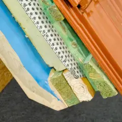 Warstwowa konstrukcja dachu z widoczną folią aluminiową paroizolacyjną, izolacją, drewnem i dachówką.