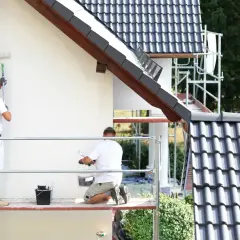 Dwóch malarzy na rusztowaniu odnawia elewację domu. Zastanawiasz się, ile kosztuje malowanie elewacji?
