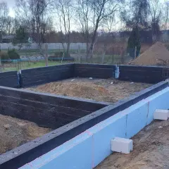 Budowa domu w toku. Widoczne fundamenty z bloczków betonowych i styropianu, przygotowane do dalszych prac.