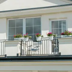 Białe okna pięknie komponują się z jasną, tynkowaną elewacją, tworząc elegancki wygląd. Balkon ozdobiony kwiatami dodaje uroku.