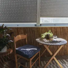 Przytulny balkon typu loggia z drewnianym krzesłem, stolikiem i roślinami.