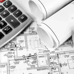 Kalkulator i zwinięte plany budowlane, sugerujące planowanie koszt instalacji elektrycznej.