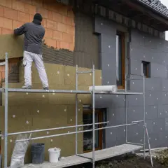 Budowlaniec montuje płyty izolacyjne na ścianie domu. To kluczowy etap prac, by wybrać odpowiedni **styropian na elewację**.
