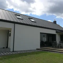 Nowoczesny dom z szarym dachem z blachy na rąbek stojący. Dach wygląda na nowy, bez widocznych wad, z dwoma oknami dachowymi.
