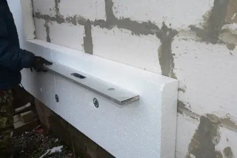 Ręczne układanie styropianu na nierównym podłożu, z użyciem poziomicy do precyzyjnego montażu.