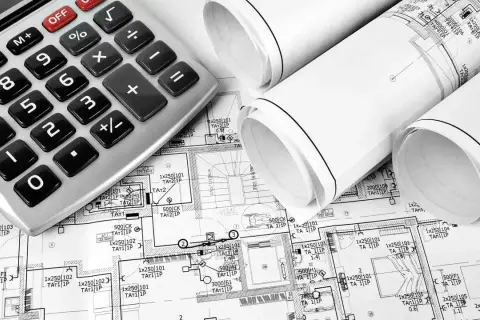 Kalkulator i zwinięte plany budowlane, sugerujące planowanie koszt instalacji elektrycznej.