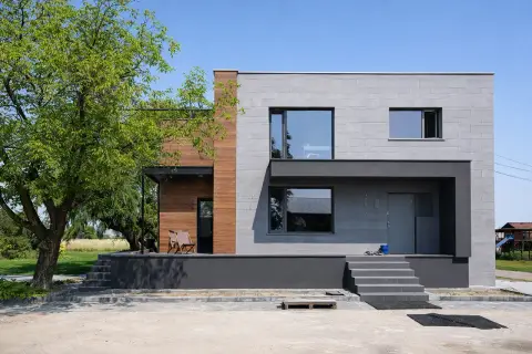 Nowoczesny dom kostka z betonową elewacją i drewnianymi akcentami. Elegancka, minimalistyczna bryła.