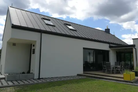 Nowoczesny dom z szarym dachem z blachy na rąbek stojący. Dach wygląda na nowy, bez widocznych wad, z dwoma oknami dachowymi.