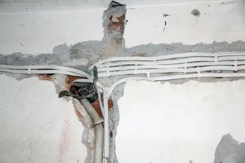 Widoczne przewody elektryczne w peszlach, częściowo odsłonięta puszka instalacyjna. Instalacja aluminiowa w trakcie prac.