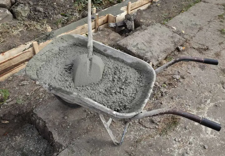 Taczka z betonem i łopatą, gotowa do wylania ławy fundamentowej. Wymiary ławy fundamentowej są kluczowe dla stabilności konstrukcji.