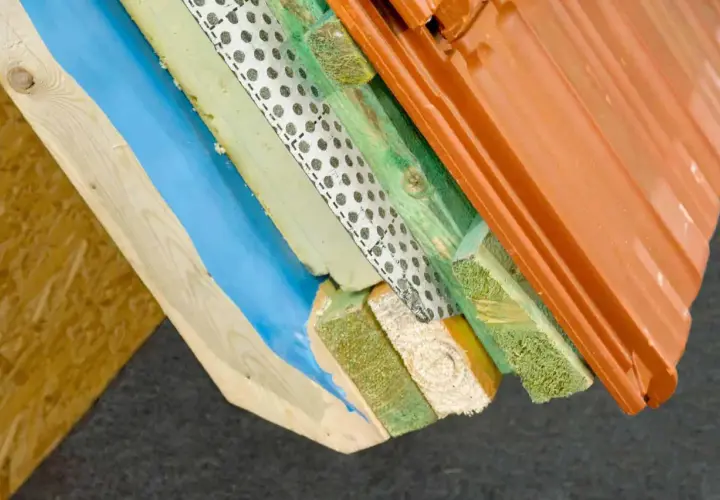 Warstwowa konstrukcja dachu z widoczną folią aluminiową paroizolacyjną, izolacją, drewnem i dachówką.