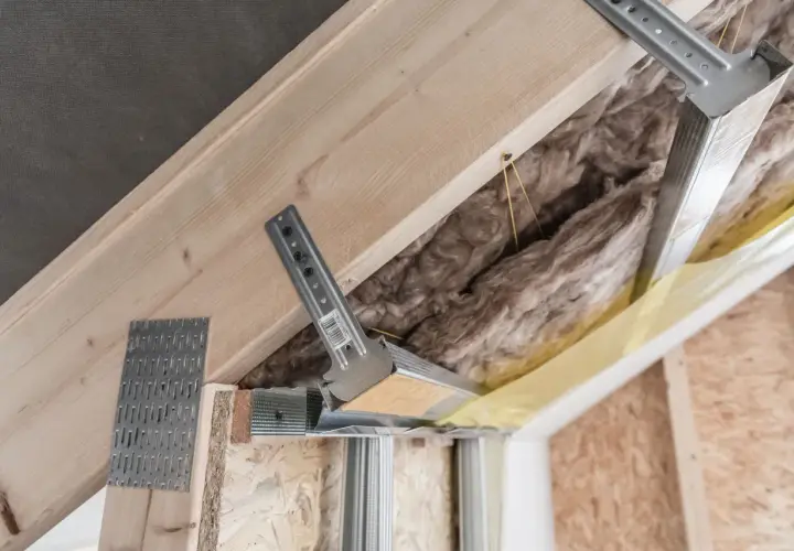 Montaż wieszaków es do krokwi. Metalowe elementy konstrukcyjne mocowane do drewnianych belek, przygotowanie pod izolację i wykończenie poddasza.