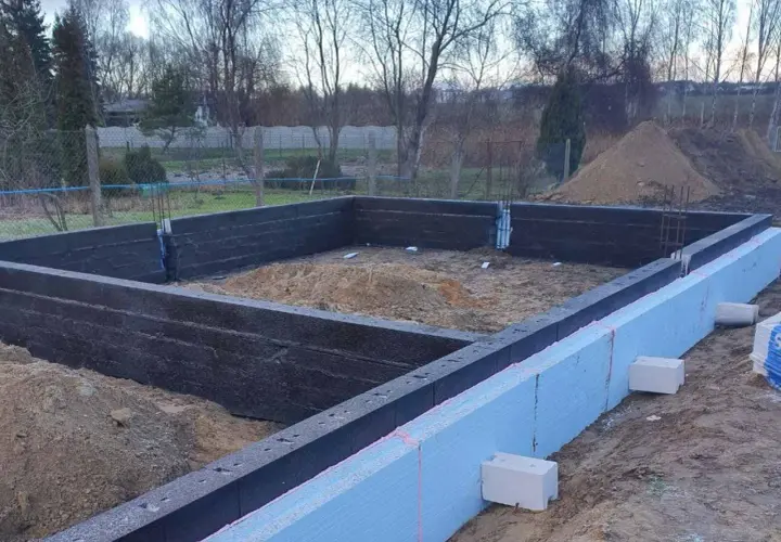 Budowa domu w toku. Widoczne fundamenty z bloczków betonowych i styropianu, przygotowane do dalszych prac.