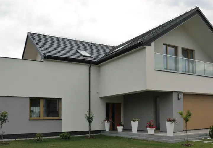 Nowoczesny dom z dwoma rodzajami elewacji: jasnoszarą i białą. Dach pokryty ciemną dachówką.