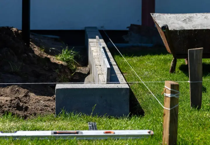 Budowa solidnego, jak głęboki fundament pod ogrodzenie. Widać betonowe bloczki, poziomicę i sznur geodezyjny.