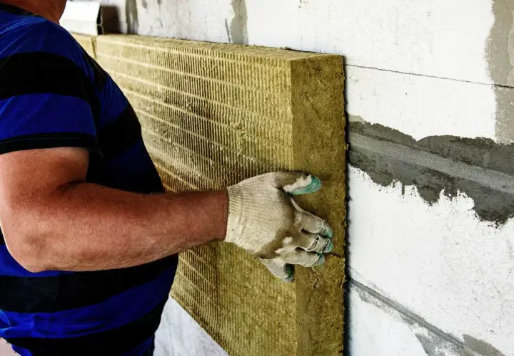 Pracownik montuje wełnę mineralną na ścianie. Utylizacja wełny mineralnej cena jest ważna przy planowaniu prac.