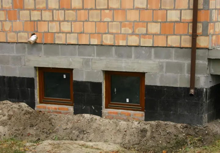 Wzmocnienie fundamentów w starym domu: nowe okna piwniczne, izolacja i warstwa cegieł.
