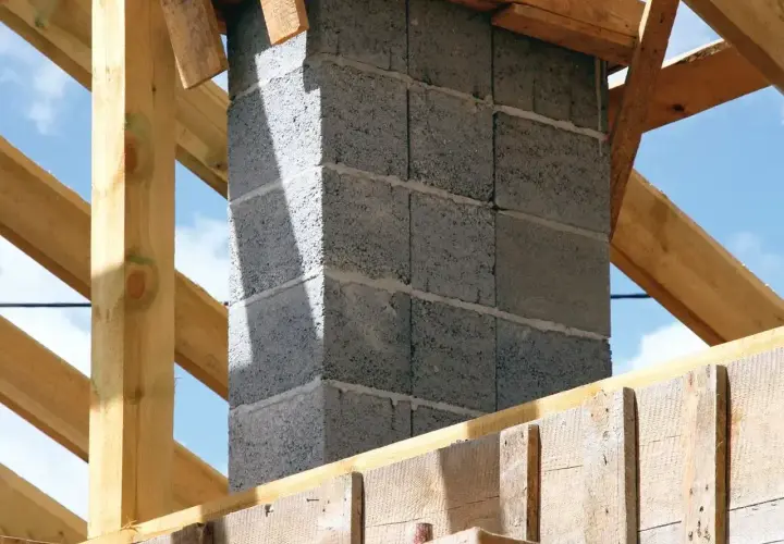 Budowa komina systemowego. Fundament z bloczków betonowych, otoczony drewnianą konstrukcją dachu.