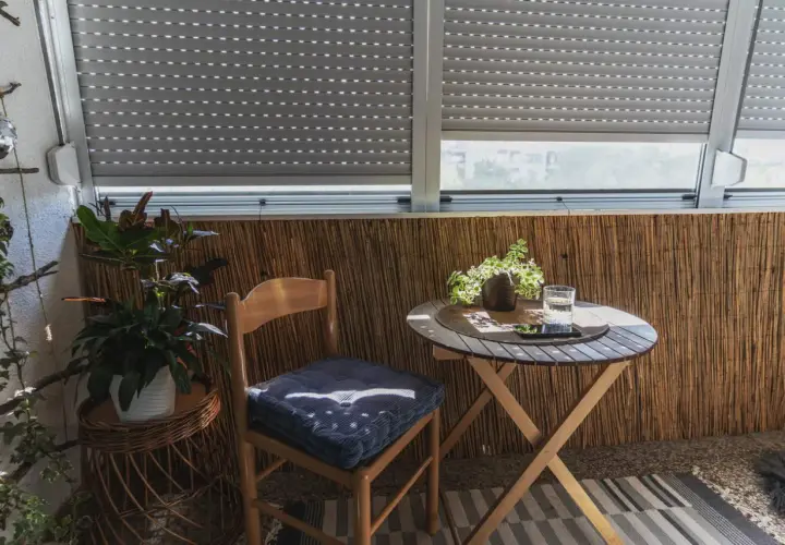 Przytulny balkon typu loggia z drewnianym krzesłem, stolikiem i roślinami.