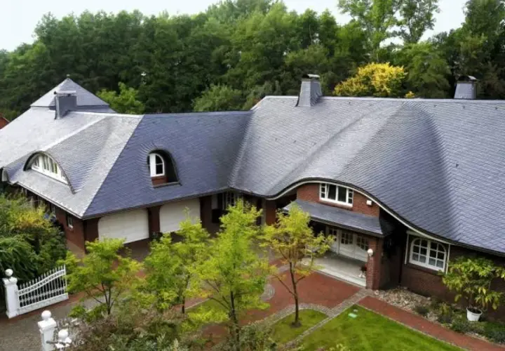 Elegancki dom z cegły z charakterystycznym, falującym dachem łupkowym, otoczony zielenią i drzewami.