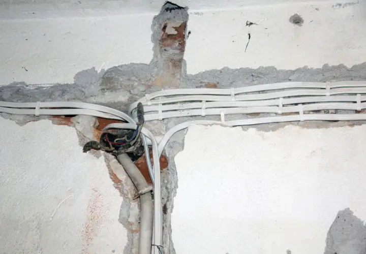 Widoczne przewody elektryczne w peszlach, częściowo odsłonięta puszka instalacyjna. Instalacja aluminiowa w trakcie prac.