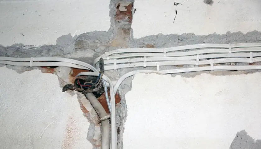 Widoczne przewody elektryczne w peszlach, częściowo odsłonięta puszka instalacyjna. Instalacja aluminiowa w trakcie prac.