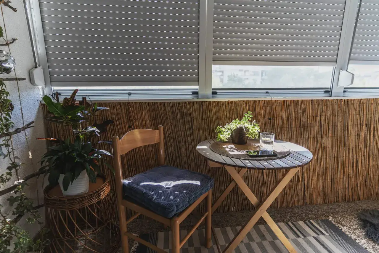 Przytulny balkon typu loggia z drewnianym krzesłem, stolikiem i roślinami.