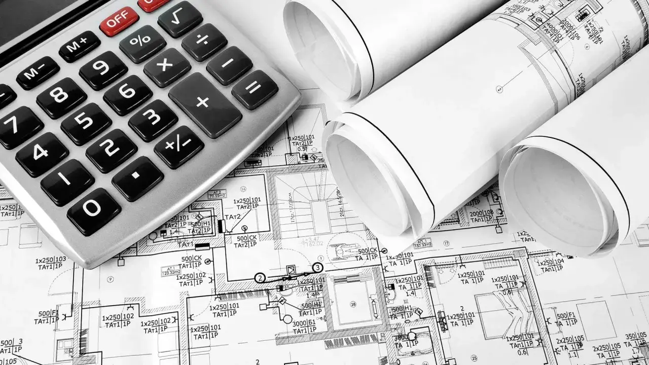 Kalkulator i zwinięte plany budowlane, sugerujące planowanie koszt instalacji elektrycznej.