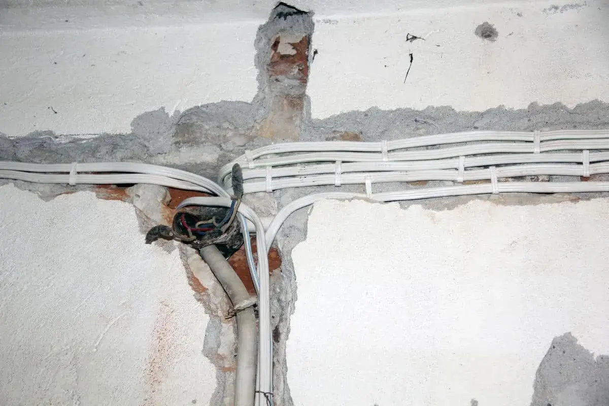 Widoczne przewody elektryczne w peszlach, częściowo odsłonięta puszka instalacyjna. Instalacja aluminiowa w trakcie prac.