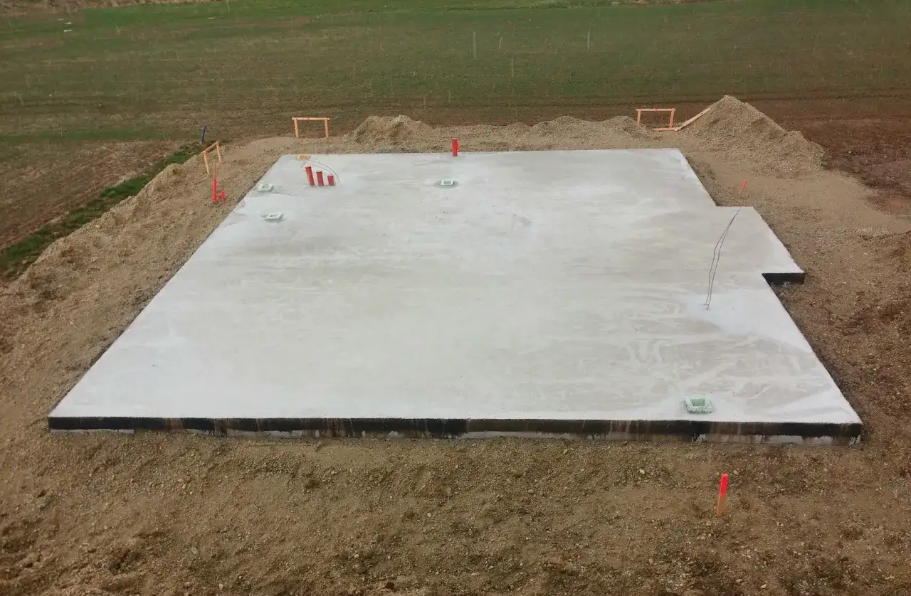 Gotowa płyta fundamentowa na budowie, otoczona ziemią i elementami instalacji.